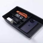 Black organizer tray holding a smartphone, car key with brown leather case, and white charger.