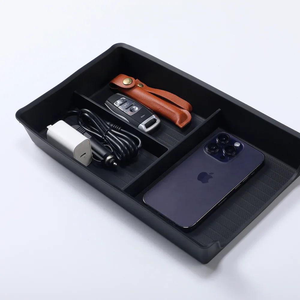 Black organizer tray holding a smartphone, car key with brown leather case, and white charger.