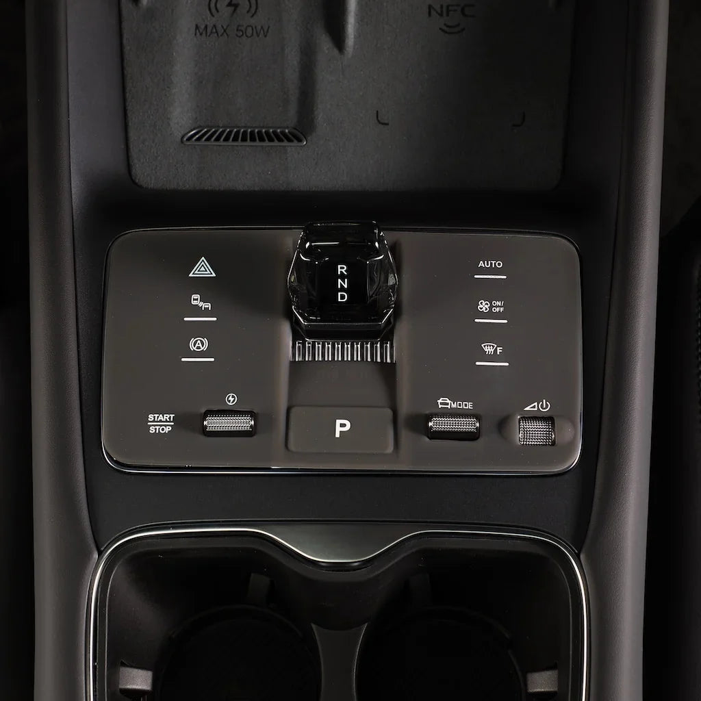 Close-up of a sleek black center console with a rotary gear shifter and touch controls.
