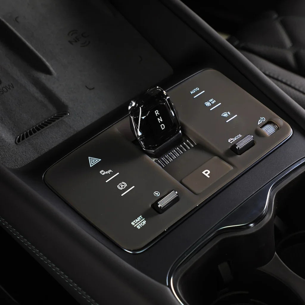 Close-up of a sleek, black glossy gear selector on a brown leather-textured center console.