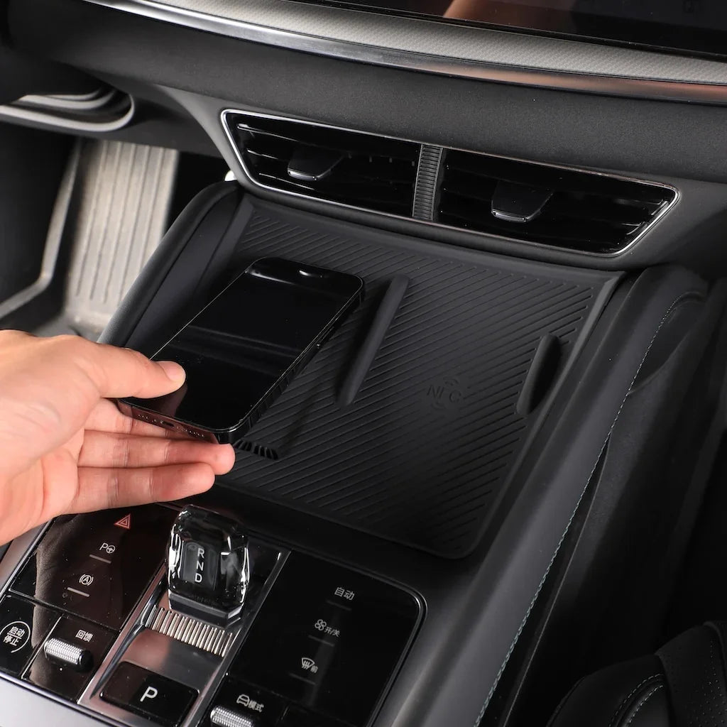 A hand places a black smartphone onto a black silicone non-slip dashboard organizer in a car interior.
