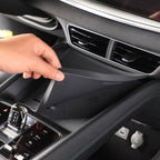 A hand lifting a black non-slip silicone dashboard mat inside a car interior.