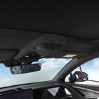 Interior view of a car showing the dark fabric headliner and rearview mirror against a bright sky.