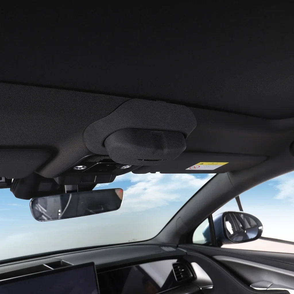 Interior view of a car showing the dark fabric headliner and rearview mirror against a bright sky.
