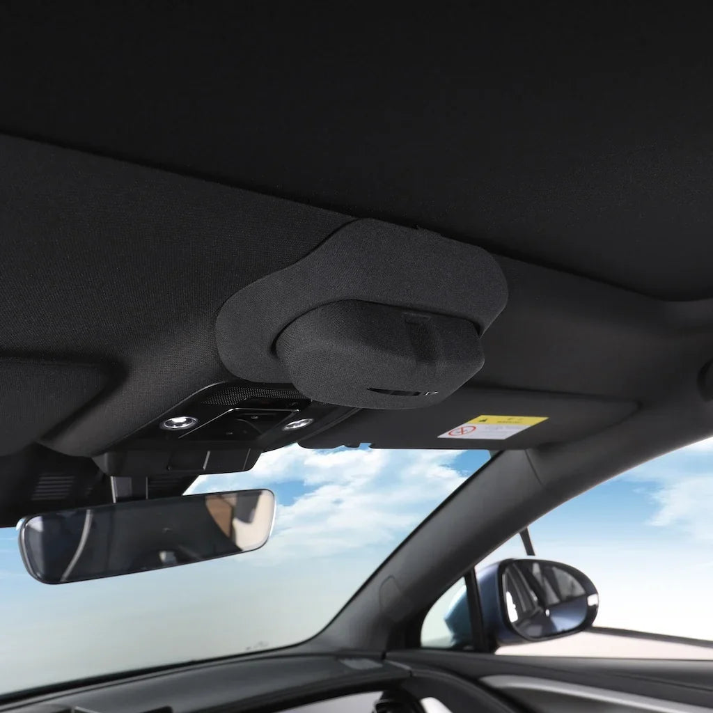 Interior view of a car ceiling featuring a dark grey fabric headliner and rearview mirror against a bright sky.