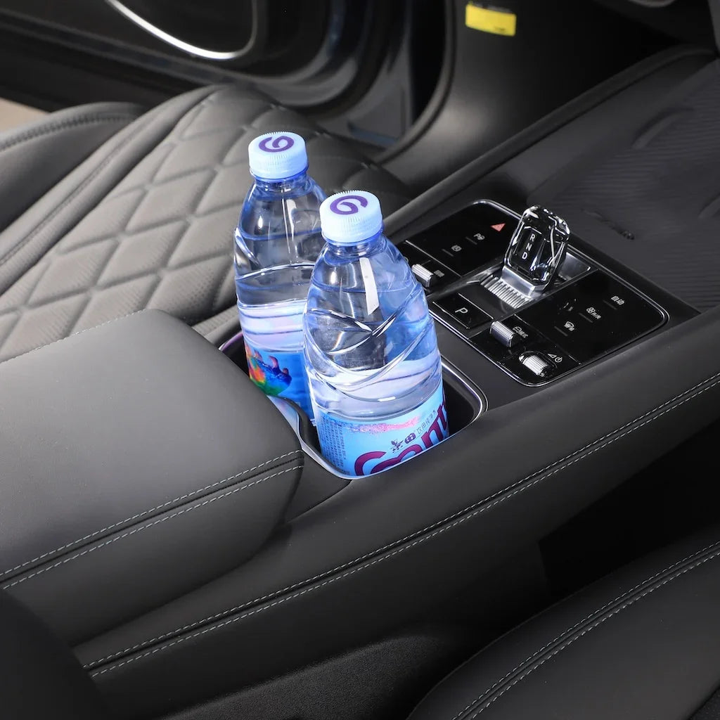 Black leather interior featuring a built-in car cup holder containing two clear plastic water bottles.
