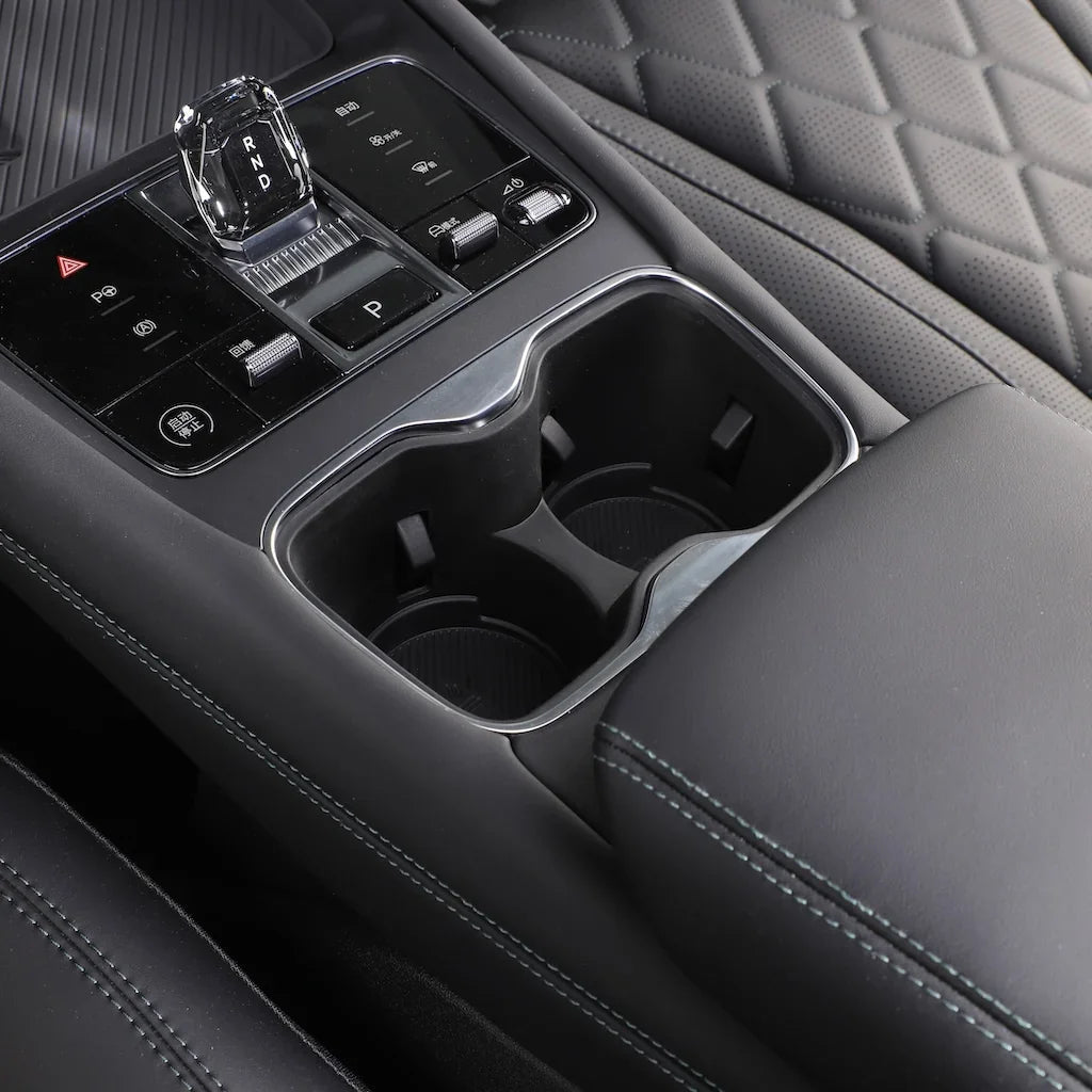 Black leather car center console with dual cup holders and chrome gear shifter.
