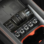 Carbon fiber texture gear shifter and control panel with silver metallic buttons in a black interior.