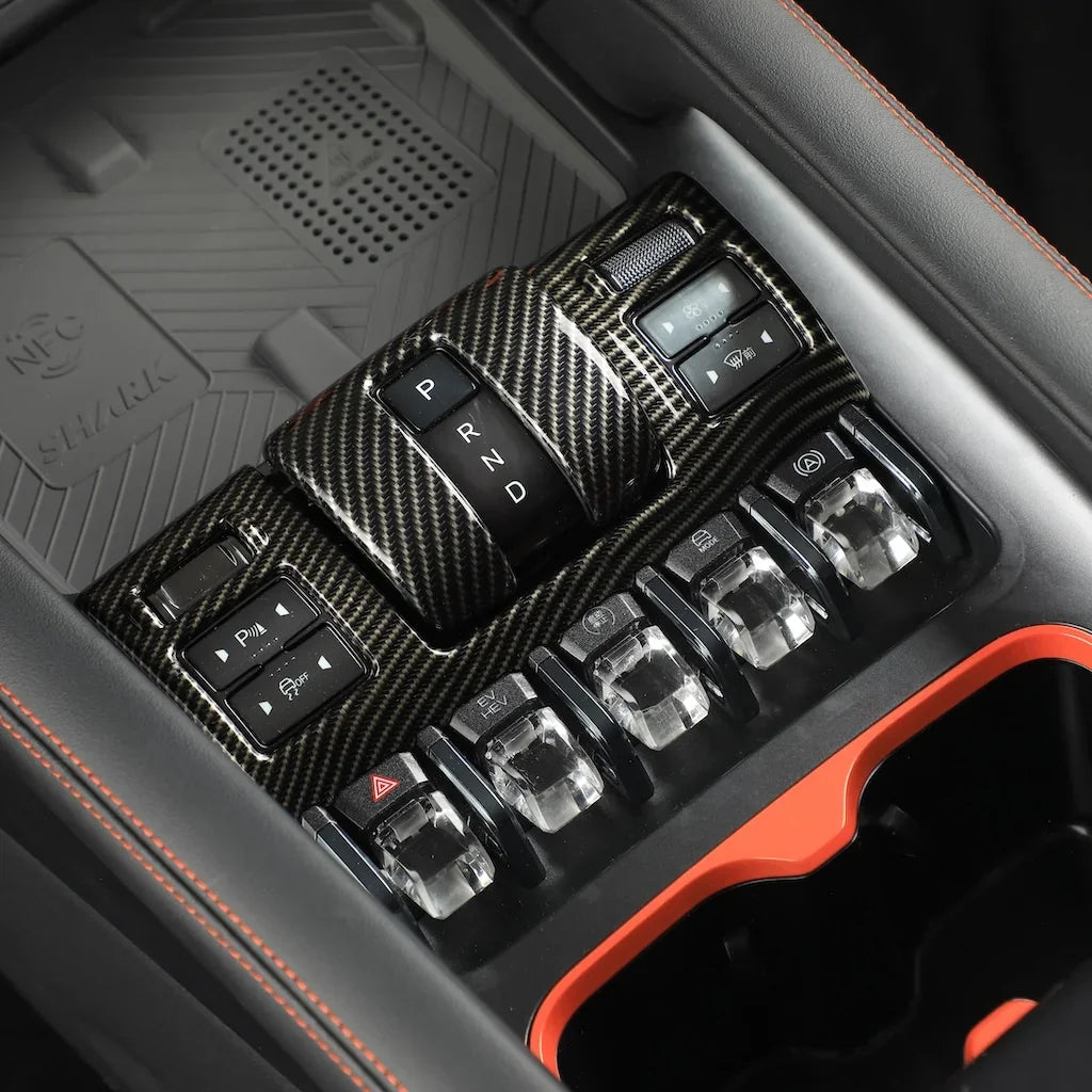 Carbon fiber texture gear shifter and control panel with silver metallic buttons in a black interior.
