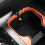 Black car center console cup holder with vibrant orange trim and protective rubber mat.