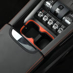 Black leather center console with orange stitching and a red-trimmed dual cup holder organizer.