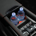 Two blue-capped water bottles in a black leather center console cup holder with red stitching.