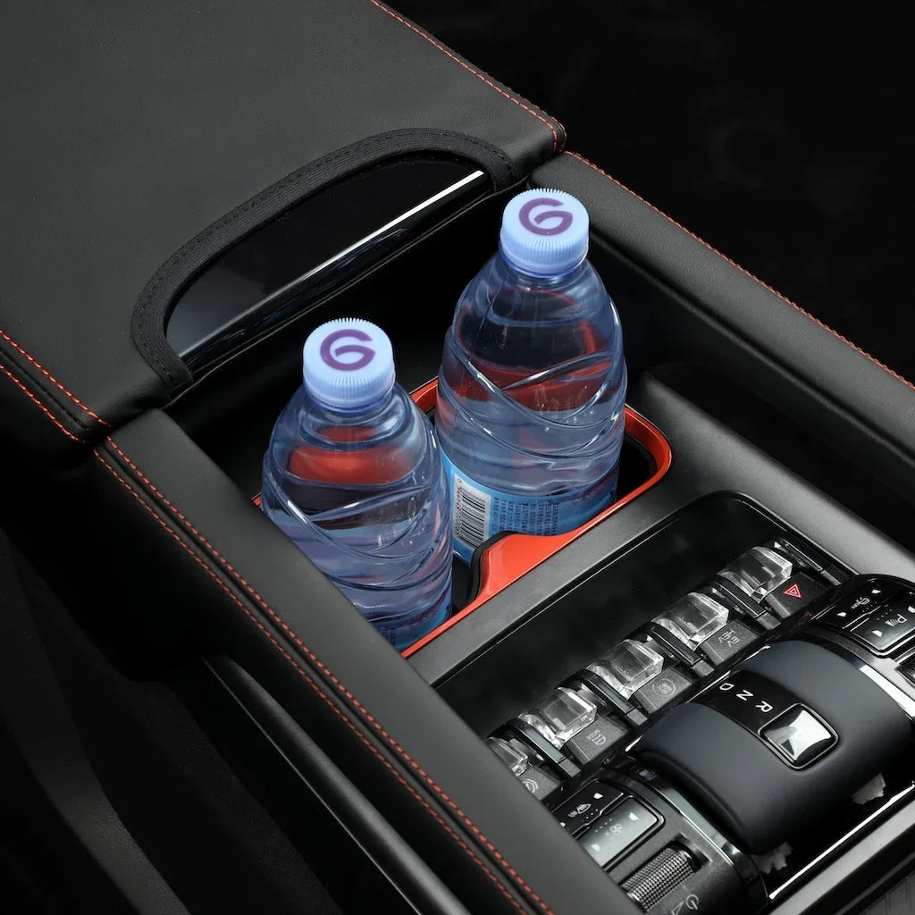 Two blue-capped water bottles in a black leather center console cup holder with red stitching.
