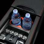 Two water bottles in a black leather center console organizer with red stitching and orange trim.