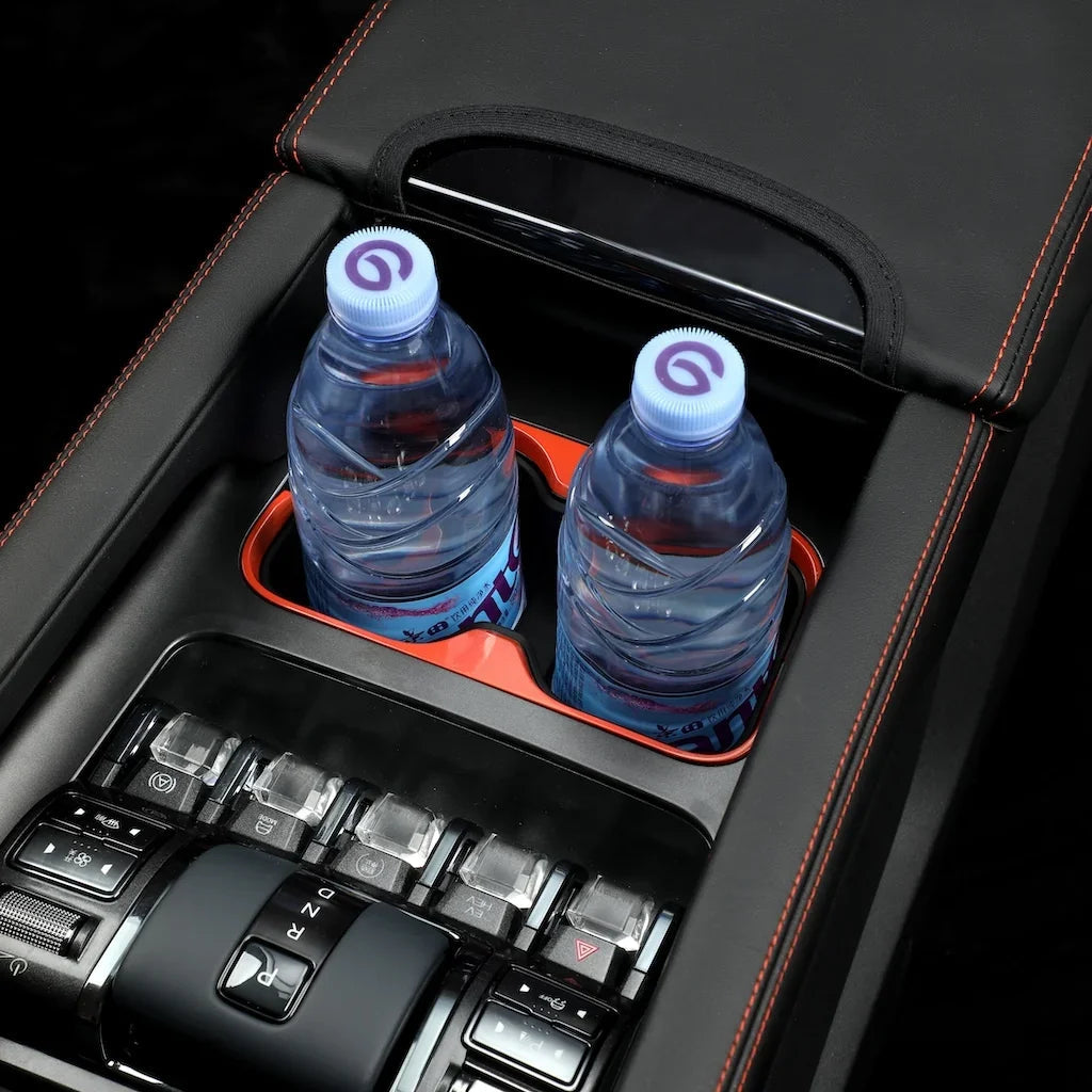 Two water bottles in a black leather center console organizer with red stitching and orange trim.