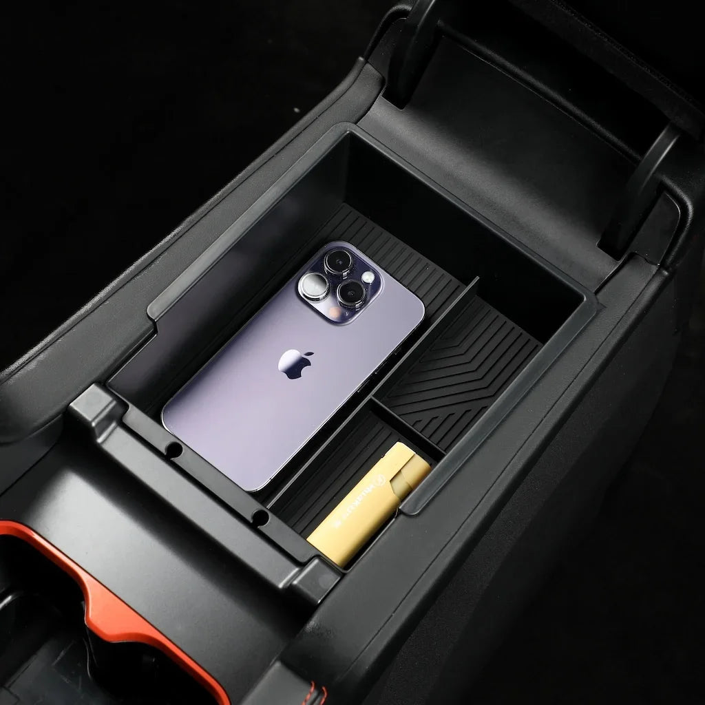 Black matte plastic center console organizer holding a purple smartphone and gold accessory.
