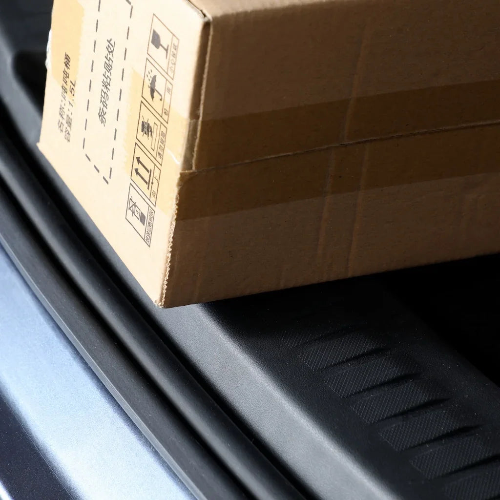 A brown cardboard shipping box placed on a black textured car trunk liner.