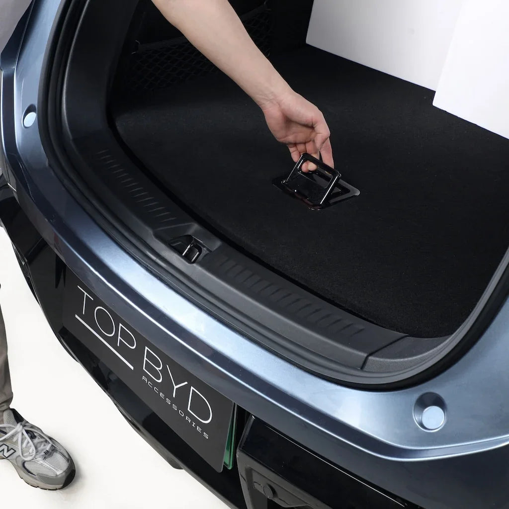 A person installing a black fabric cargo liner in the trunk of a blue BYD vehicle.