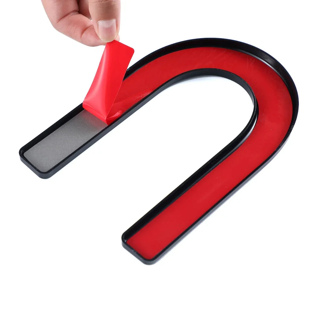 Hand peeling a red adhesive backing from a black and red horseshoe magnet.