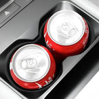 Two red beverage cans placed in a black car cup holder accessory.