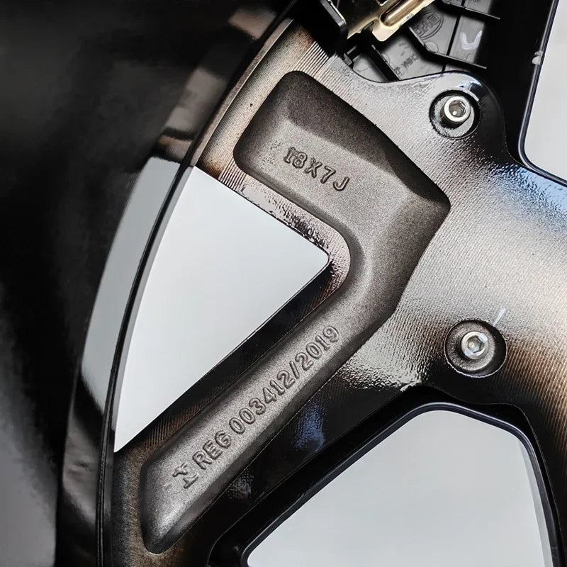 Close-up of a black metallic alloy wheel rim featuring 18X7J size specifications and registration engraving.
