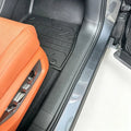 Custom-fit black rubber floor mat protecting the interior of a car with orange leather seats.