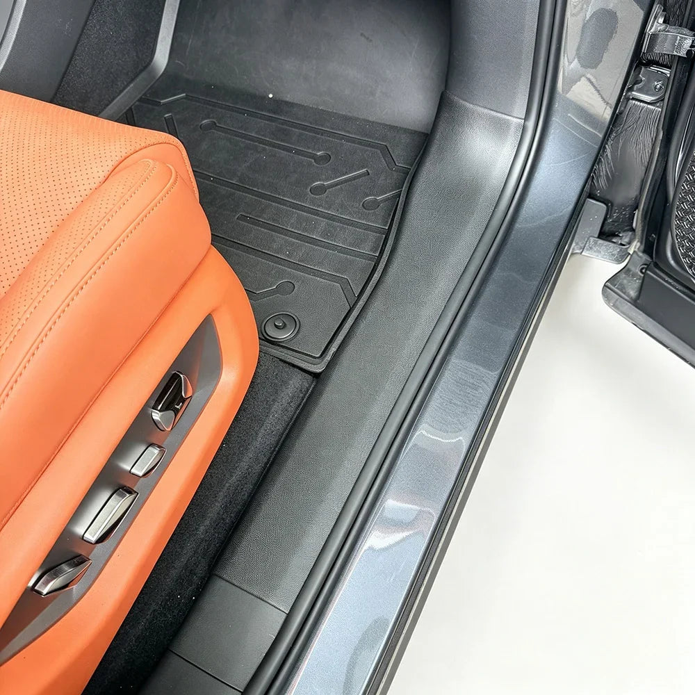Custom-fit black rubber floor mat protecting the interior of a car with orange leather seats.