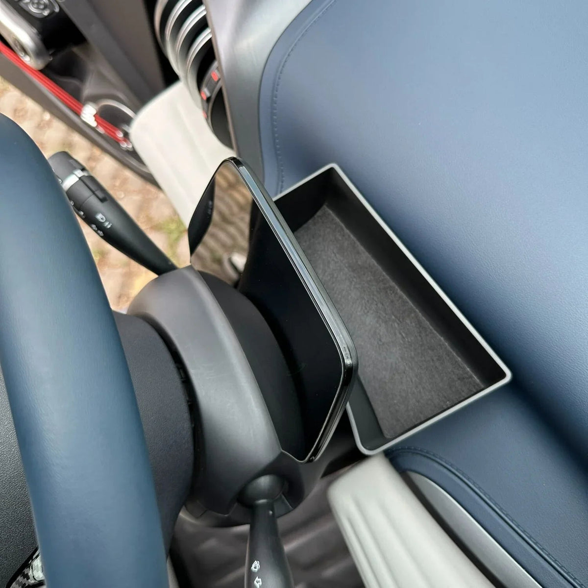 Black smartphone mounted on a sleek dashboard holder within a blue car interior.