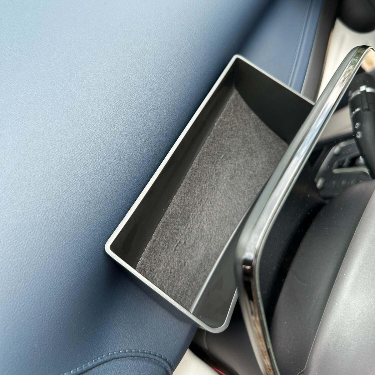 Black rectangular storage tray with a grey felt lining installed in a blue car interior console.