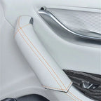 White leather car armrest cover with contrasting orange stitching for interior protection.
