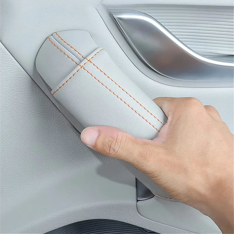 Grey leather car door handle cover with orange contrast stitching being held by a hand.