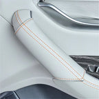 White leather car interior armrest cover with contrasting orange stitching.