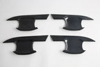 Set of four black carbon fiber texture interior trim panels for car door protection.