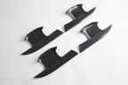 Four black carbon fiber door trim covers with a glossy textured finish.
