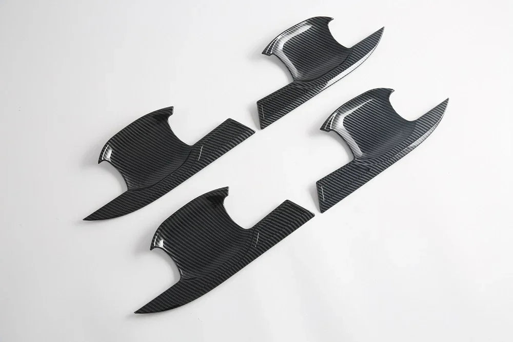 Four black carbon fiber door trim covers with a glossy textured finish.