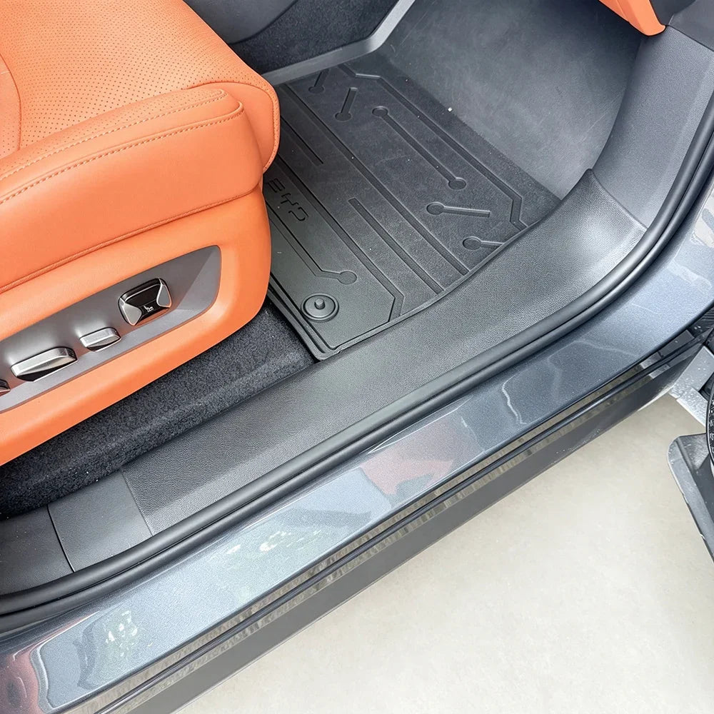 Custom-fit black rubber floor mat installed in a car with orange leather seats.
