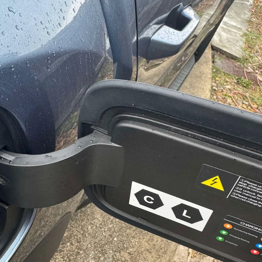 Black matte protective cover for BYD electric vehicle charging port with safety warning labels.