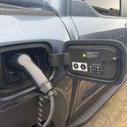 Close-up of a black electric vehicle charging plug inserted into a grey car's charging port.
