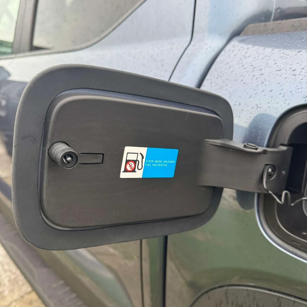 Black matte fuel filler door cover with a blue and white fuel type warning sticker.