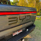Glossy black BYD emblem on the grey tailgate of a BYD Shark pickup truck.
