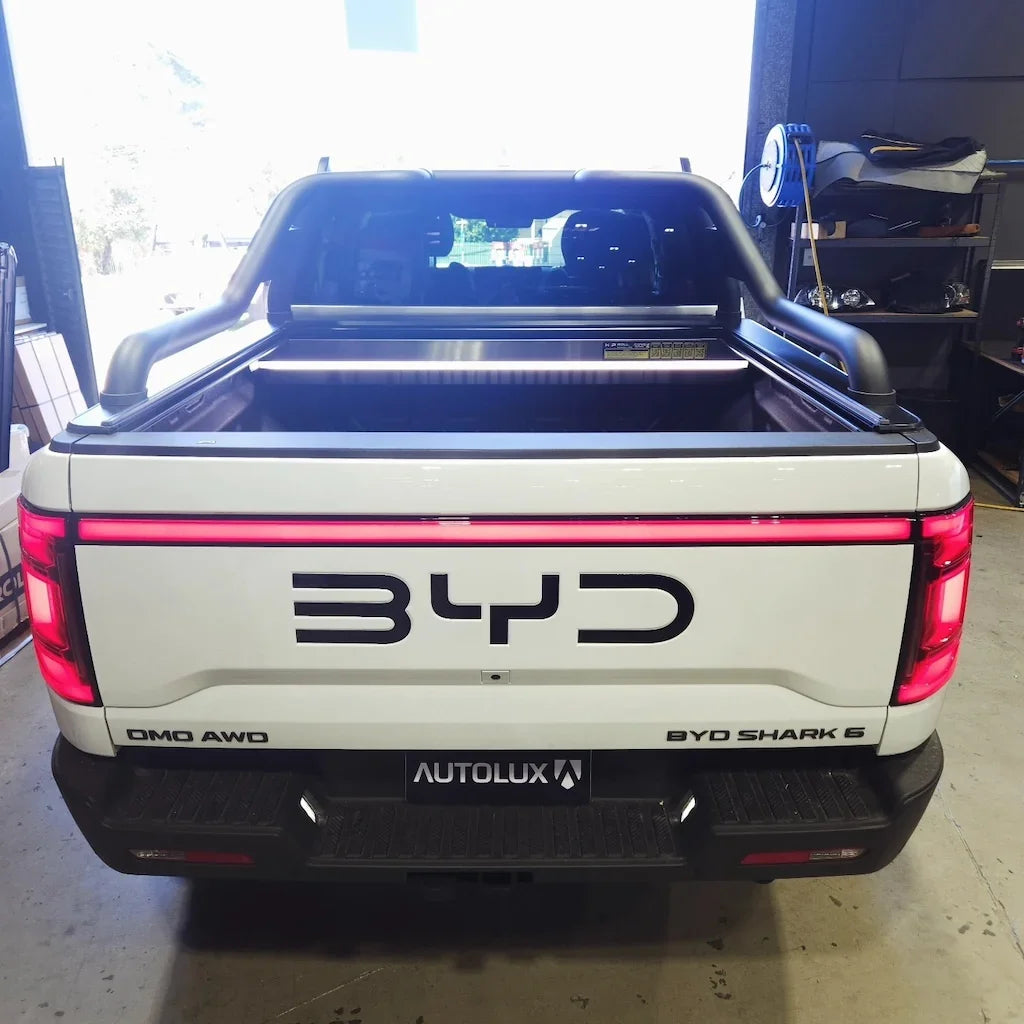 Rear view of a white BYD Shark 6 pickup truck with a black roll bar and integrated LED light bar.