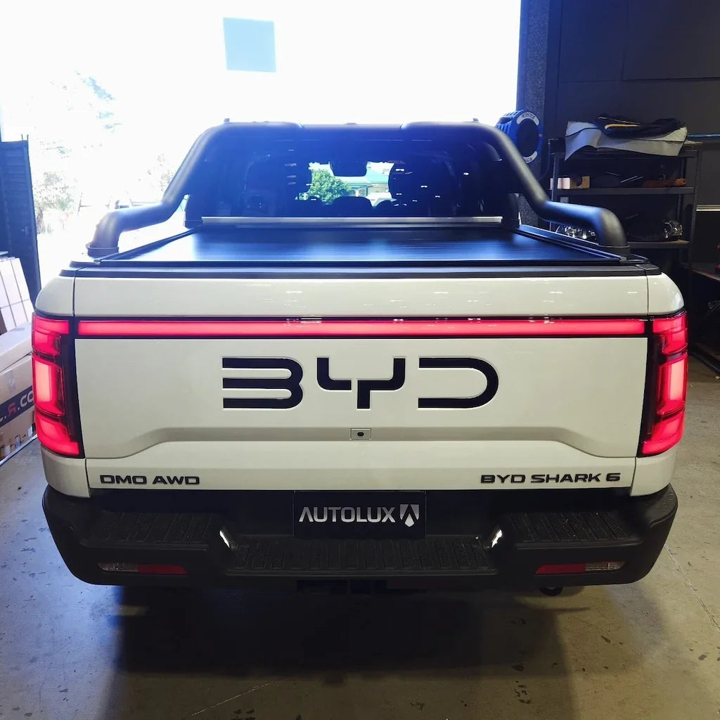 Rear view of a white BYD Shark 6 electric pickup truck featuring a black roll bar and integrated LED tail light bar.