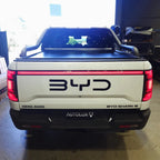 Rear view of a white BYD Shark 6 electric pickup truck featuring a black roll bar and integrated LED tail light bar.