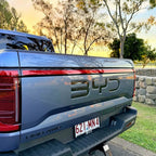 Rear view of a blue BYD DMO AWD pickup truck parked outdoors during sunset.