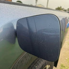 Water droplets on a sleek, dark grey matte finish side mirror of a vehicle.