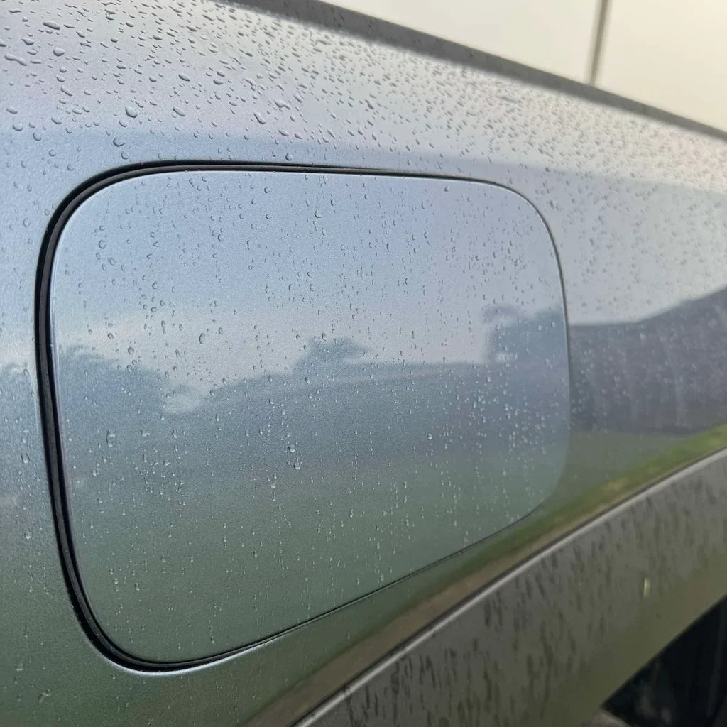 Close-up of a grey metallic car body with water droplets on the fuel filler door.