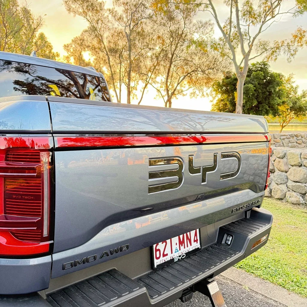 Rear view of a grey BYD Shark pickup truck featuring a sleek black BYD emblem and red LED taillights.