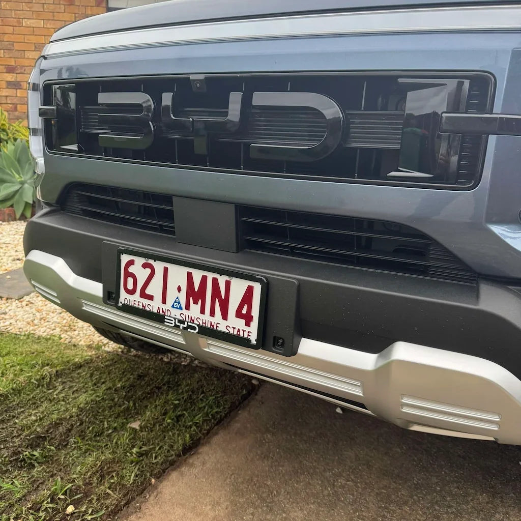 Glossy black BYD front grille with bold lettering on a grey vehicle bumper.