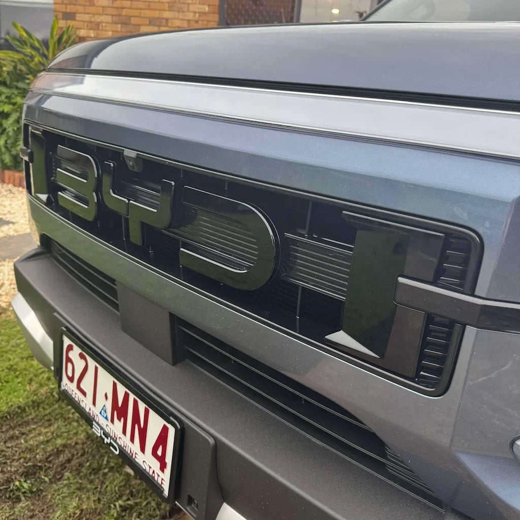 Glossy black BYD emblem and textured grille on a grey BYD vehicle front bumper.