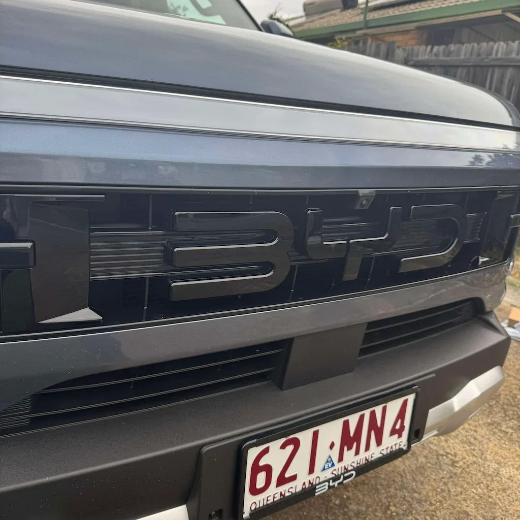 Glossy black BYD emblem integrated into a sleek grey car front grille.